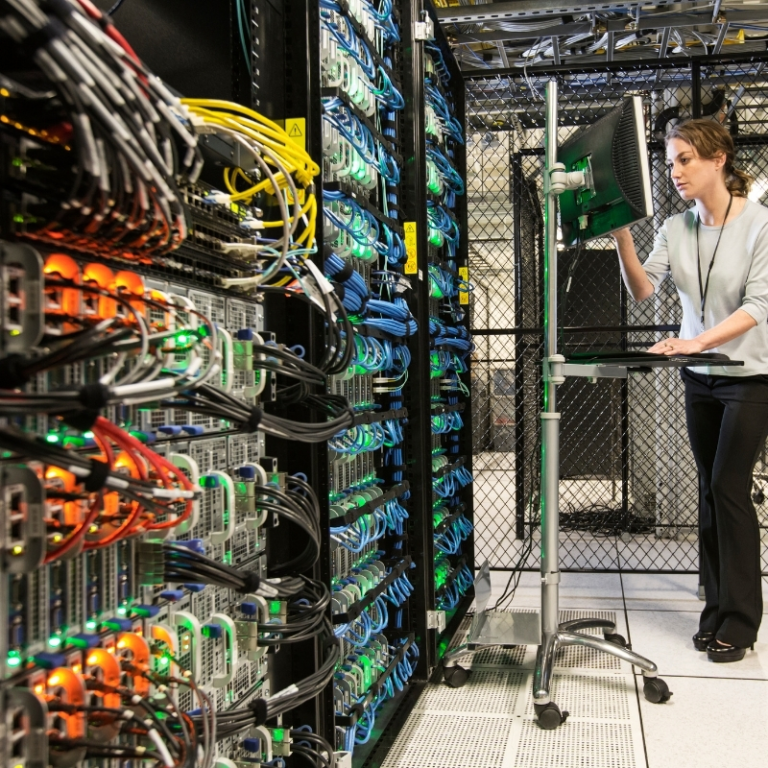 A female IT professional is working in a server room with many ethernet cables.