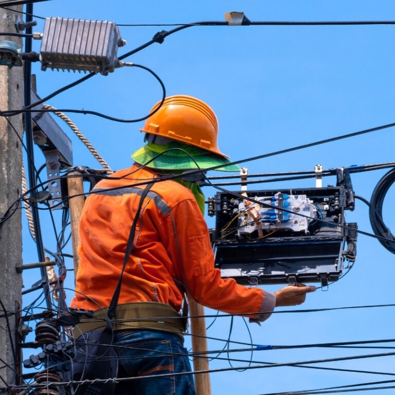 A telecommunications employee is working on cabling on a tower.